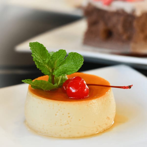 A flan dessert topped with a maraschino cherry and mint leaves on a white plate.