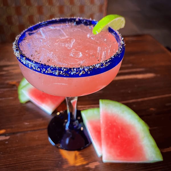 Watermelon margarita with a lime wedge and salted rim, served with watermelon slices on a wooden table.