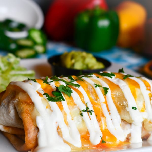 A Tacos El Tio burrito, topped with melted cheese, sour cream, and cilantro, with guacamole and peppers.