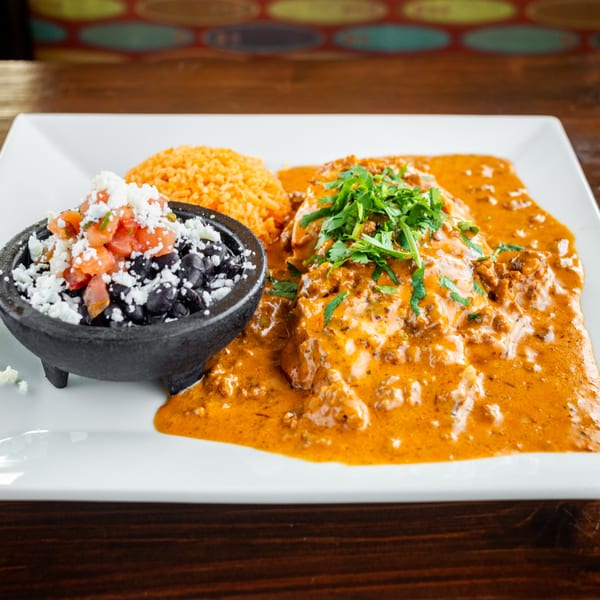 Mexican dish with meat in orange sauce, rice, and black beans topped with pico de gallo and cheese.