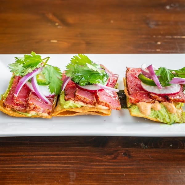 Three Tacos El Tio tostadas with seared tuna, guacamole, red onion, jalapeño, and cilantro.