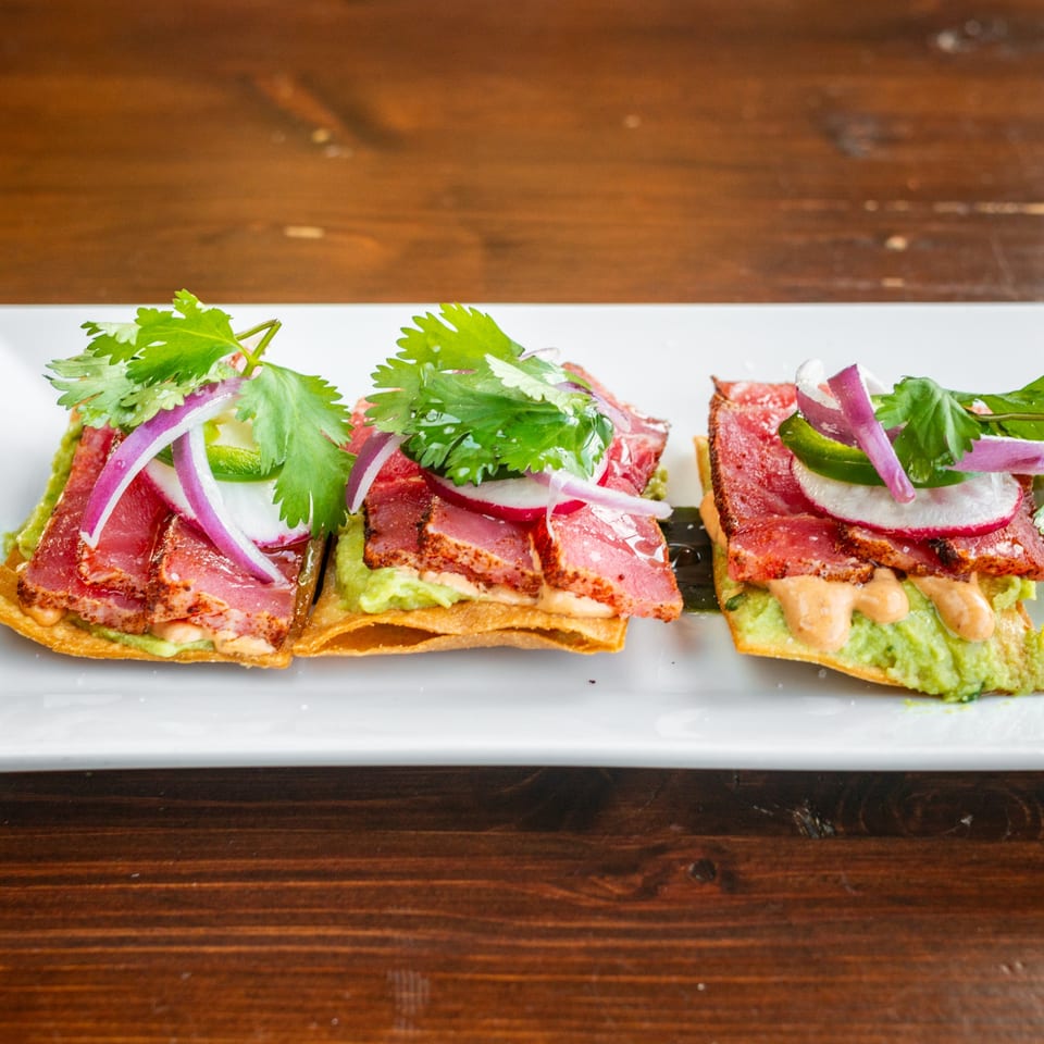 Three Tacos El Tio tostadas with seared tuna, guacamole, red onion, jalapeño, and cilantro.