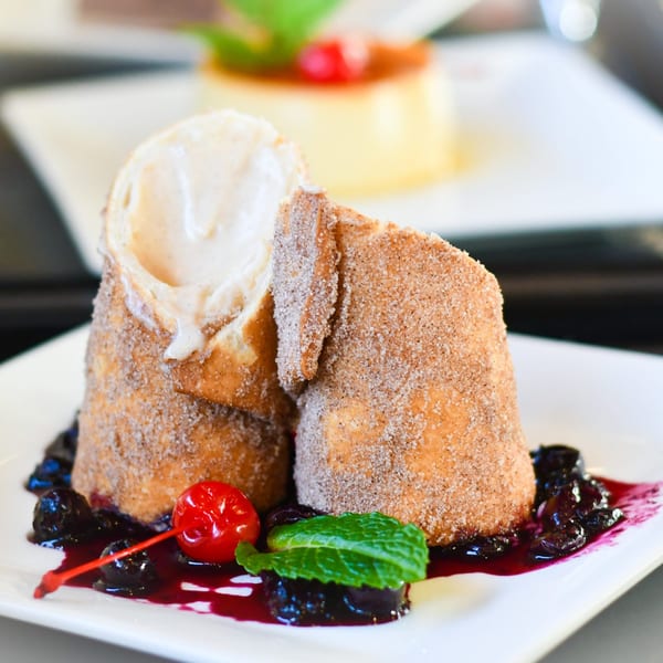 Two churro desserts with ice cream, cherry, mint, and blueberry sauce on a white plate.