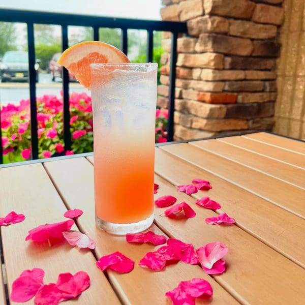 A refreshing grapefruit cocktail with a salted rim and pink petals on a wooden outdoor table.