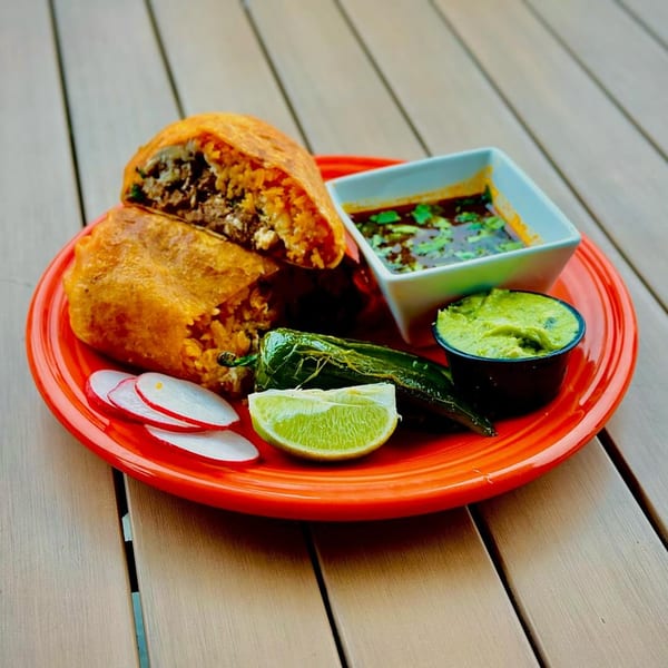 A Mexican burrito cut in half, revealing meat and rice, served with salsa, guacamole, and lime.