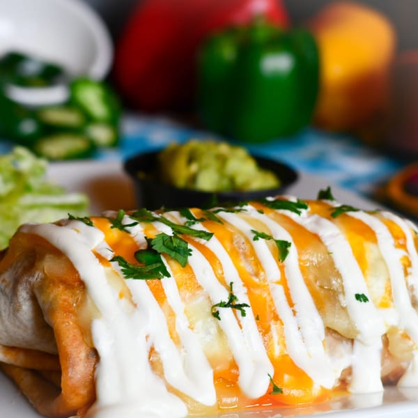 A large, golden-brown burrito topped with white sour cream, melted cheese, and green cilantro.