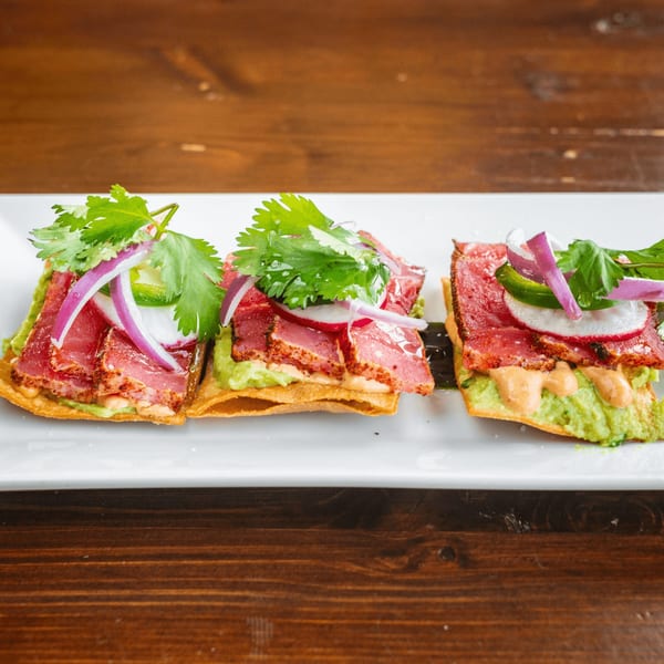 Three Tacos El Tio tostadas with seared tuna, guacamole, red onion, cilantro, and sauce.