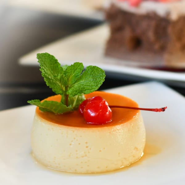 Flan dessert with caramel topping, a maraschino cherry, and mint sprig on a white plate.