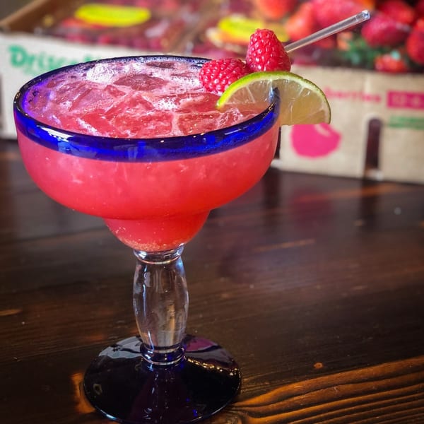 Raspberry margarita with lime and raspberries in a blue-rimmed glass on a wooden table.