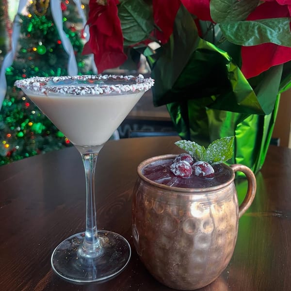 Two festive cocktails, a martini and a copper mug drink, on a table with Christmas decorations.
