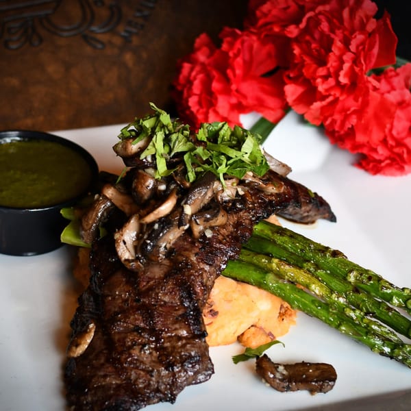 Grilled steak with mushrooms, cilantro, asparagus, and a side of green sauce, with red flowers.