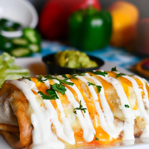 A Tacos El Tio burrito, topped with melted cheese, sour cream, and fresh cilantro, with guacamole.