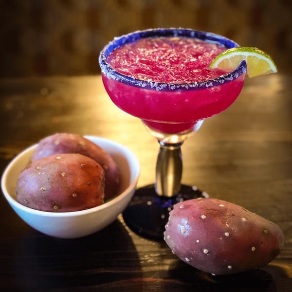 Prickly pear margarita with a lime wedge and salt rim, next to a bowl of fresh prickly pears.